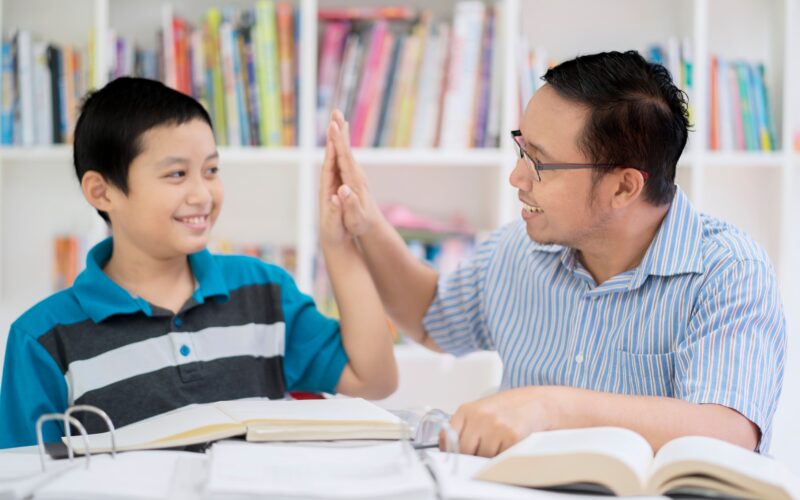 Portrait of an Asian male teacher doing high five with his student while studying together in the library